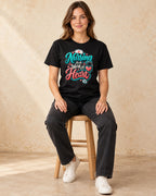 Model seated Nursing Is A Work Of Heart T-shirt in Black