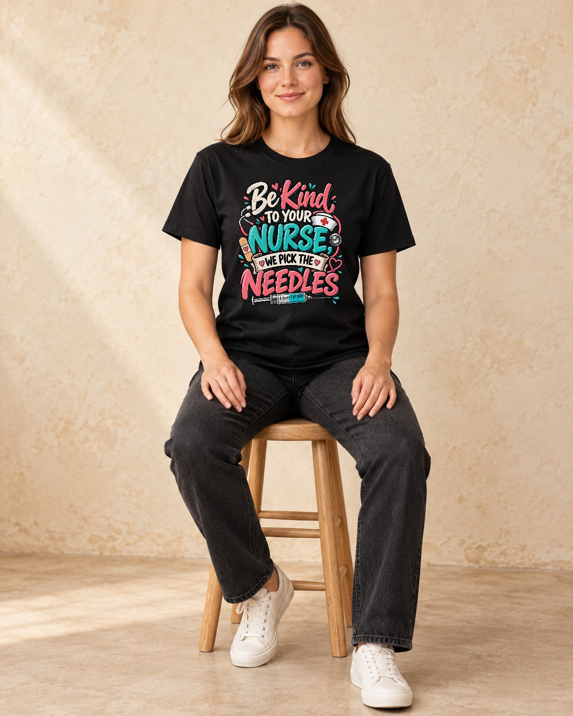Model seated Be Kind To Your Nurse We Pick The Needles T-shirt in Black